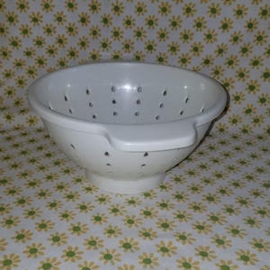 Peut inclure: Une passoire en plastique blanc avec de nombreux petits trous de drainage. La passoire a une poign&eacute;e d'un c&ocirc;t&eacute; et est pos&eacute;e sur un fond &agrave; motifs floraux. Cet ustensile de cuisine est con&ccedil;u pour &eacute;goutter les liquides des aliments.