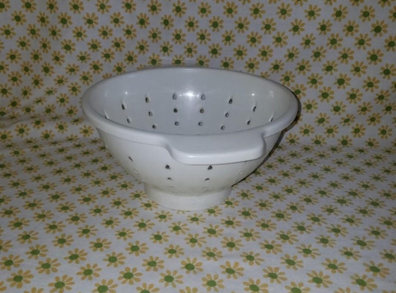 Peut inclure: Une passoire en plastique blanc avec de nombreux petits trous de drainage. La passoire a une poign&eacute;e d'un c&ocirc;t&eacute; et est pos&eacute;e sur un fond &agrave; motifs floraux. Cet ustensile de cuisine est con&ccedil;u pour &eacute;goutter les liquides des aliments.