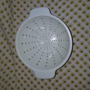 Peut inclure: Une passoire en plastique blanc avec deux poign&eacute;es. La passoire comporte de nombreux petits trous pour &eacute;goutter les liquides. La passoire est ronde et poss&egrave;de un bord l&eacute;g&egrave;rement &eacute;vas&eacute;. C'est un ustensile de cuisine.