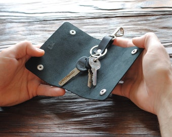 May include: A black leather key holder with a silver key ring and three keys. The key holder is open and the keys are visible.