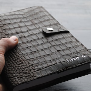May include: A brown leather journal with a crocodile embossed pattern. The journal has a silver button closure and is personalized with the name "Soleny A."