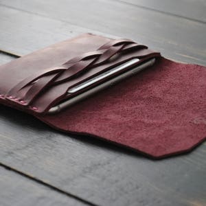 May include: A burgundy leather phone case with a braided design. The case is open and a smartphone is visible inside.