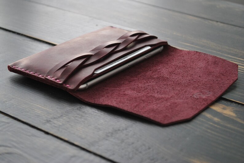 May include: A burgundy leather phone case with a braided design. The case is open and a smartphone is visible inside.