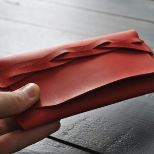 May include: A red leather wallet with a braided design. The wallet is closed and has a flap.