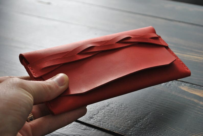 May include: A red leather wallet with a braided design. The wallet is closed and has a flap.