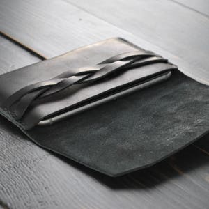 May include: A black leather phone case with a braided strap. The case is open and the phone is visible inside.
