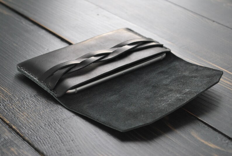 May include: A black leather phone case with a braided strap. The case is open and the phone is visible inside.