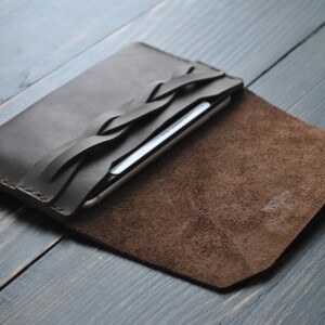 May include: A brown leather phone case with a braided leather strap. The case is open and the inside is lined with brown suede.