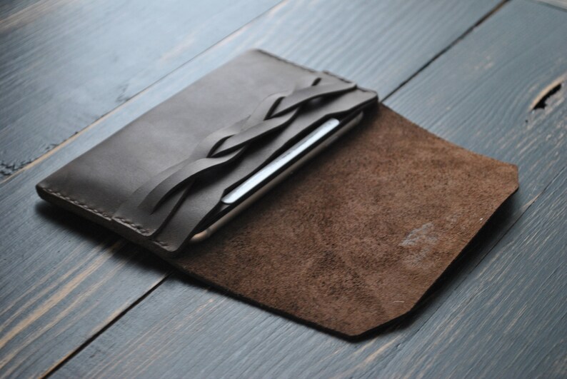 May include: A brown leather phone case with a braided leather strap. The case is open and the inside is lined with brown suede.