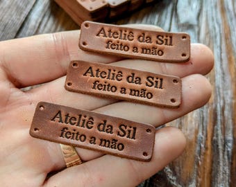 Può includere: Tre etichette in pelle marrone con il testo "Ateliê da Sil feito a mão" in rilievo.