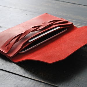 May include: Red leather wallet with a braided design and a phone and credit card inside.