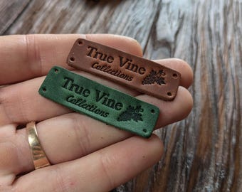 Può includere: Due etichette in pelle con il testo "True Vine Collections" e un design a vite. L'etichetta superiore è marrone e l'etichetta inferiore è verde.