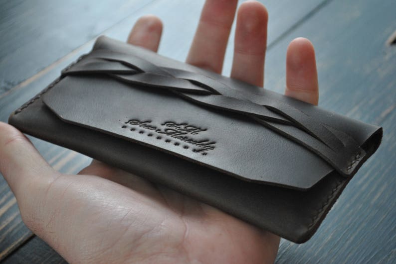 May include: A dark brown leather wallet with a braided design and the text "The Artfully" embossed on the front.