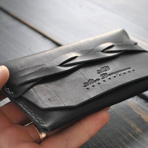 May include: A black leather wallet with a braided strap and the text "Alice Demers" embossed on the front.