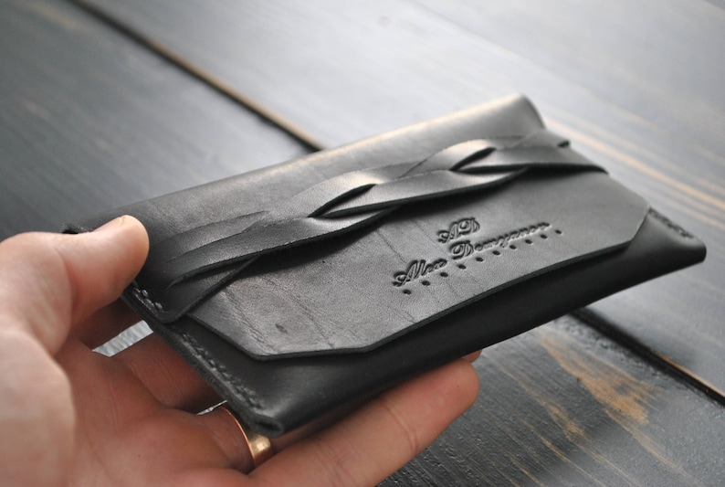 May include: A black leather wallet with a braided strap and the text "Alice Demers" embossed on the front.