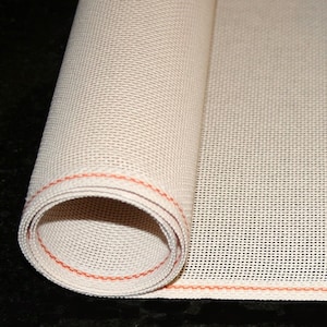 May include: A rolled-up beige mesh fabric with a red stitched border. The fabric has a woven texture, possibly for crafting or protection. The image shows a close-up of the rolled edge and the open weave, revealing the fabric's construction.