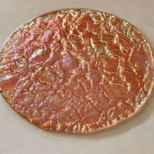 May include: A round, iridescent glass plate with a textured surface. The plate has a gold and orange color scheme.