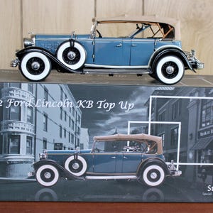 May include: A blue 1932 Ford Lincoln KB Top Up model car with white-walled tires and a tan convertible top. The model sits on a box with a similar car image and the text "1932 Ford Lincoln KB Top Up".