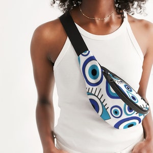 May include: A white fanny pack with a blue and white evil eye pattern. The fanny pack has a black adjustable strap and a zipper closure.