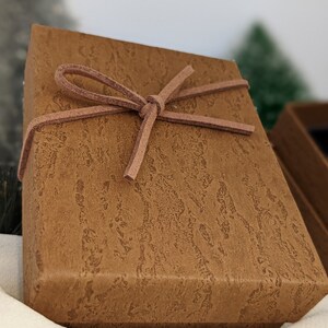 May include: A brown gift box with a brown leather ribbon tied in a bow. The box has a textured surface that resembles wood.