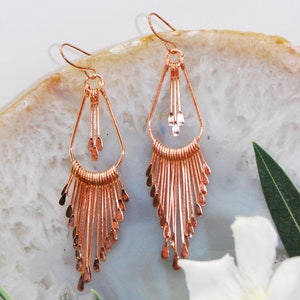 May include: A pair of rose gold dangle earrings with a teardrop shape and a fringe of delicate wire strands.