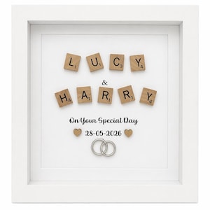 May include: A white framed wedding gift featuring the names "LUCY & HARRY" in wooden letter tiles. The text "On Your Special Day" and the date "28-05-2026" are below the names, along with two hearts and two intertwined rings.
