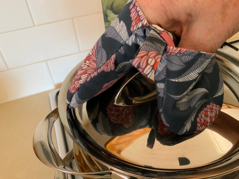 May include: A hand wearing a floral print oven mitt is holding the lid of a stainless steel pot.