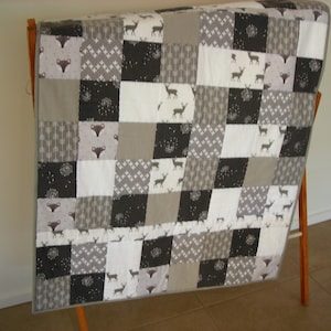 May include: A patchwork quilt in shades of grey, white, and black. The quilt showcases deer, foxes, and geometric patterns. The quilt is displayed on a wooden clothes airer. The quilt's dimensions are not visible.