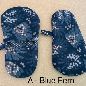 May include: A pair of blue oven mitts with a white floral pattern. The mitts have a hanging loop and a heat-resistant lining. The text "A - Blue Fern" is printed below the mitts.