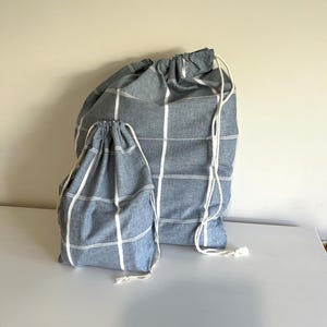 May include: Two blue and white striped drawstring bags of different sizes. The bags are made of fabric and have white drawstrings. The bags are on a white surface.