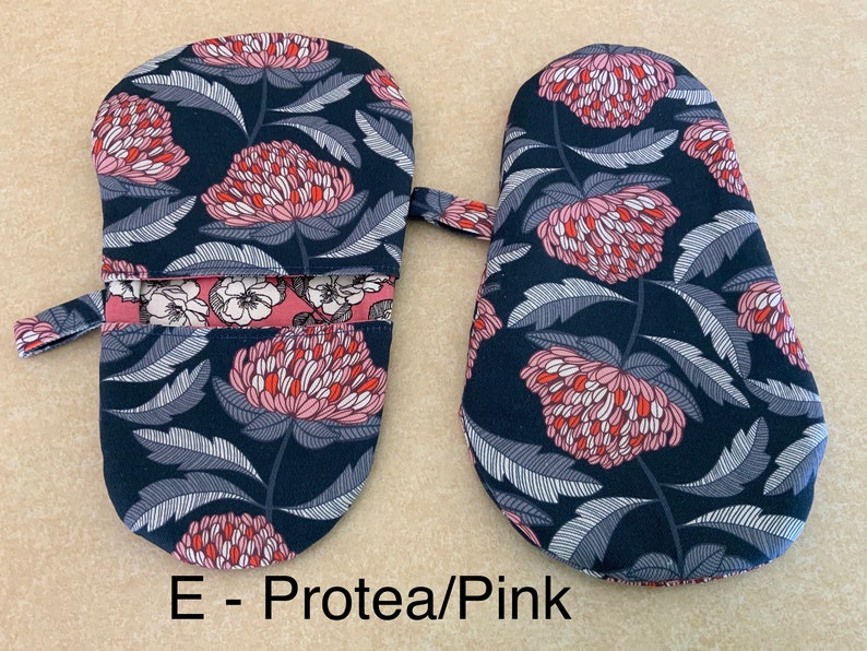 May include: A pair of oven mitts with a floral print. The mitts are dark blue with pink and red flowers. The text "E - Protea/Pink" is printed below the mitts.