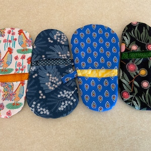 May include: Four oven mitts with different patterns. The first mitt is white with a rooster and flowers. The second mitt is blue with a floral pattern. The third mitt is blue with a teardrop pattern. The fourth mitt is black with a floral pattern.