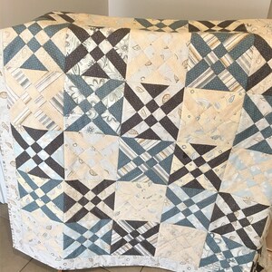 May include: A quilt made of various fabric squares in shades of blue, brown, and cream. The squares are arranged in a pattern of alternating colours and designs.