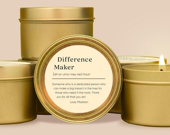Puede incluir: Latas de velas doradas con una etiqueta blanca que dice "Difference Maker [dif-er-uhns-mey-ker] noun Someone who is a dedicated person who can make a big impact in the lives for those who need it the most. Thank you for all that you do! Love, Madison"