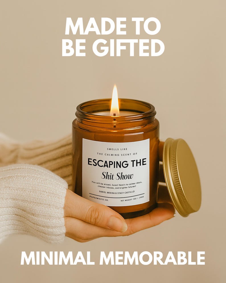 May include: A lit candle in an amber glass jar with a gold lid. The white label reads: MADE TO BE GIFTED, SMELLS LIKE THE CALMING SCENT OF ESCAPING THE Shit Show, You will be missed, Soos! Here's to calmer days, clearer inboxes, and brighter futures!, PAPERWHITE CO. NET WEIGHT 7OZ / 198G, MINIMAL MEMORABLE.