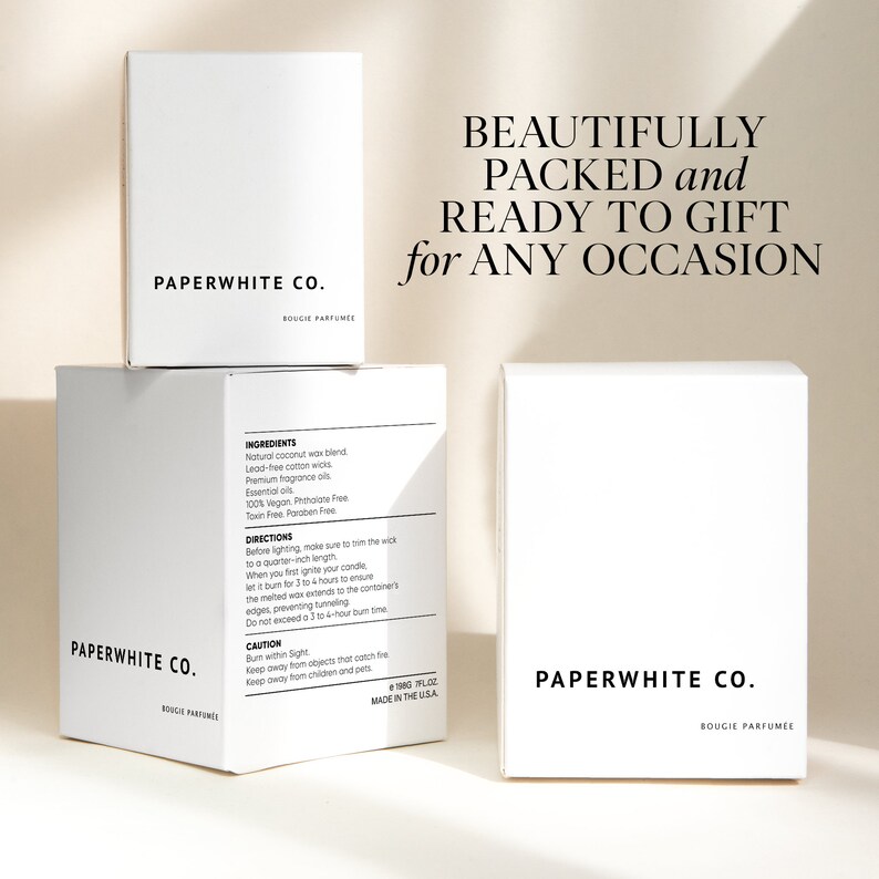 May include: Three white boxes stacked on top of each other. The top box has the text "PAPERWHITE CO. BOUGIE PARFUMEE" printed on it. The middle box has the text "PAPERWHITE CO. BOUGIE PARFUMEE" printed on it and the text "INGREDIENTS" and "DIRECTIONS" printed on the side. The bottom box has the text "PAPERWHITE CO. BOUGIE PARFUMEE" printed on it. The boxes are all on a white background. The text "BEAUTIFULLY PACKED and READY TO GIFT for ANY OCCASION" is printed in black on the white background.