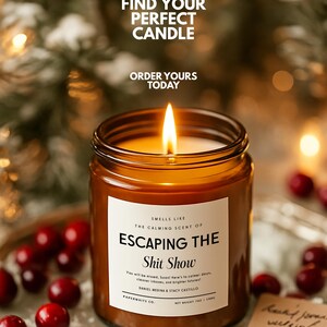 May include: A lit candle in an amber glass jar with a white label reading "SMELLS LIKE THE CALMING SCENT OF ESCAPING THE Shit Show". The label includes additional text and "NET WEIGHT 7OZ / 198G". The candle is surrounded by red cranberries.