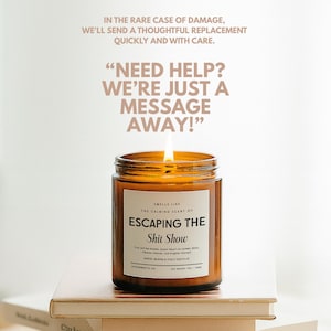 May include: A lit candle in an amber glass jar with a white label reading "SMELLS LIKE THE CALMING SCENT OF ESCAPING THE Shit Show". Text above reads "THE PAPERWHITE PROMISE" and "NEED HELP? WE'RE JUST A MESSAGE AWAY!" with policy details.