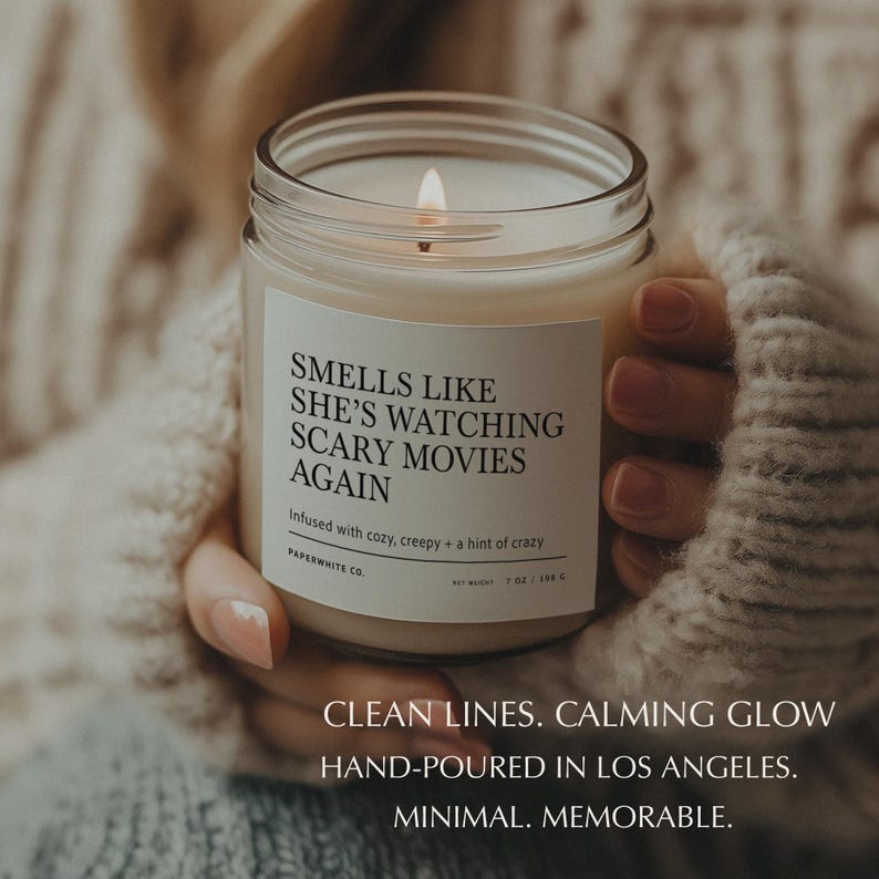 Clear jar candle close-up showing the label clearly and glowing flame in cozy, spooky lighting.