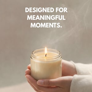 May include: A lit candle in a clear glass jar is held in cupped hands. The candle has a soft, creamy color, and the flame is bright. The text "DESIGNED FOR MEANINGFUL MOMENTS" is above the candle.