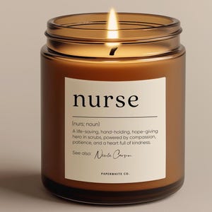 May include: A brown glass candle jar with a white label that reads "nurse (nurs; noun) A life-saving, hand-holding, hope-giving hero in scrubs, powered by compassion, patience, and a heart full of kindness. See also: Nicole Carson PAPERWHITE CO."
