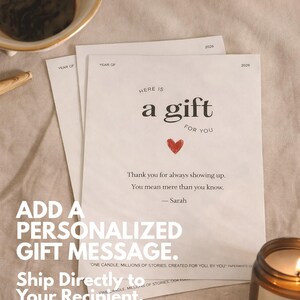 May include: A gift message card with the text "Here is a gift for you" and a red heart. The card is on a beige surface with a lit candle and a cup of coffee in the background. The card also says "Thank you for always showing up."