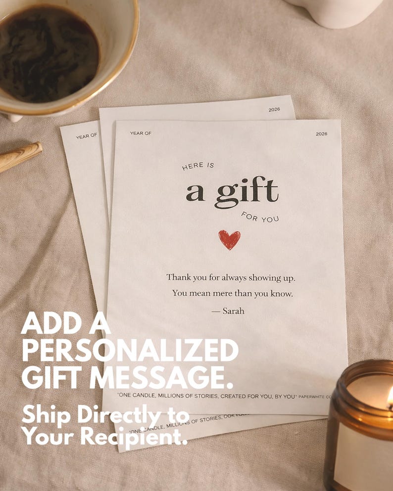 May include: A gift message card with the text "Here is a gift for you" and a red heart. The card is on a beige surface with a lit candle and a cup of coffee in the background. The card also says "Thank you for always showing up."