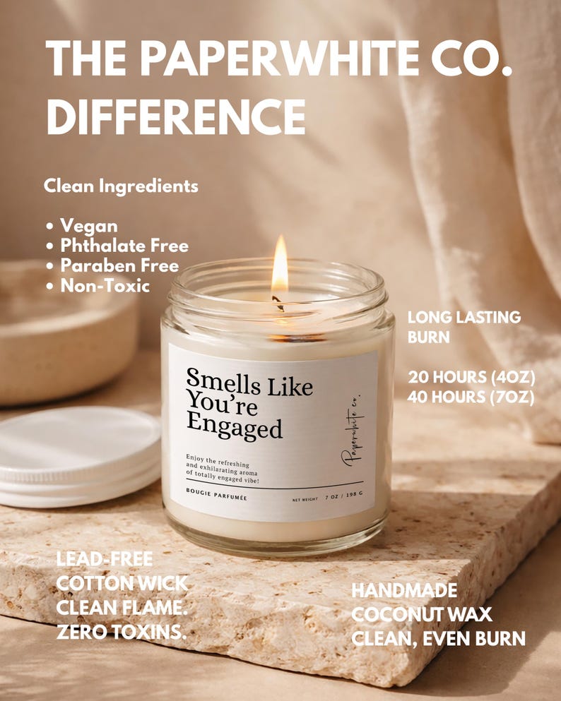 May include: A lit, clear glass jar candle with the text "Smells Like You're Engaged." The candle has a white label and a white lid. The candle is made with vegan, phthalate-free, paraben-free, and non-toxic ingredients. It has a lead-free cotton wick and a clean flame.