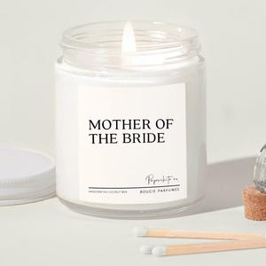 May include: White candle jar with a black label that reads "Mother of the Bride". The label also includes the text "Paperwhite co. Bougie Parfumee" and "Handcrafted Coconut Wax".