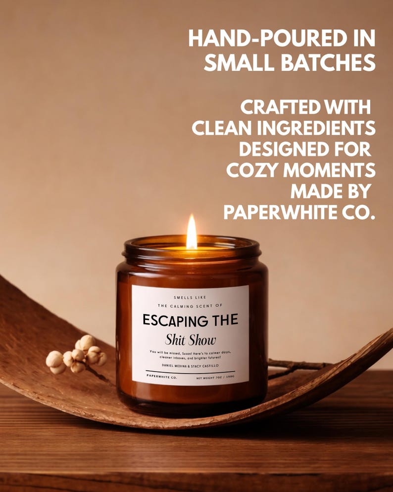 May include: A lit candle in an amber glass jar with a white label reading "SMELLS LIKE THE CALMING SCENT OF ESCAPING THE Shit Show". Text above reads "HAND-POURED IN SMALL BATCHES, CRAFTED WITH CLEAN INGREDIENTS, DESIGNED FOR COZY MOMENTS, MADE BY PAPERWHITE CO."
