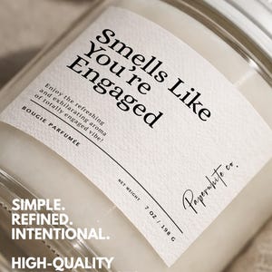 May include: A clear glass jar candle with a silver lid and a white label. The label reads "Smells Like You're Engaged" and "Paperwhite co." The candle weighs 7 oz / 198 g. The text "Simple. Refined. Intentional. High-Quality Print That Lasts." is also visible.