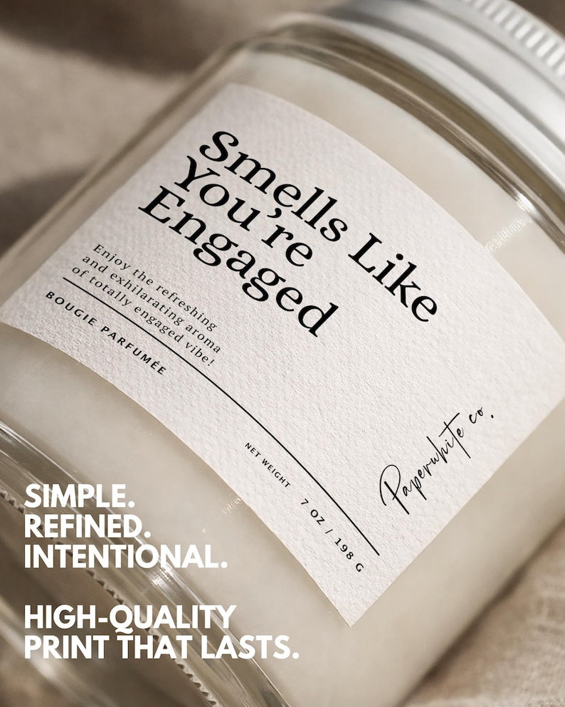 May include: A clear glass jar candle with a silver lid and a white label. The label reads "Smells Like You're Engaged" and "Paperwhite co." The candle weighs 7 oz / 198 g. The text "Simple. Refined. Intentional. High-Quality Print That Lasts." is also visible.