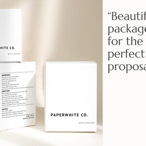 May include: White boxes with the text "PAPERWHITE CO." and "BOUCIE PARFUMES" printed in black. One box has product information. The text "Beautifully packaged for the perfect proposal" is also visible.