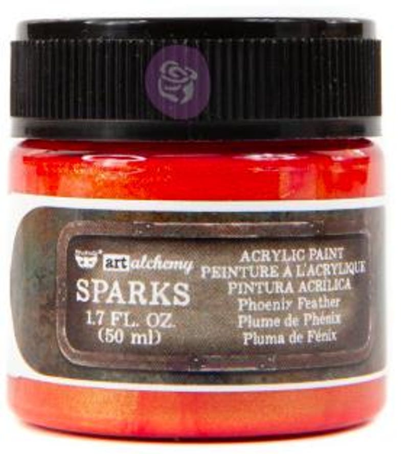 May include: A jar of Art Alchemy Sparks acrylic paint in the colour Phoenix Feather. The jar has a black ribbed lid and a label with the text Sparks, 1.7 fl. oz. (50 ml), and Phoenix Feather. The paint inside the clear glass jar is a vibrant red-orange.